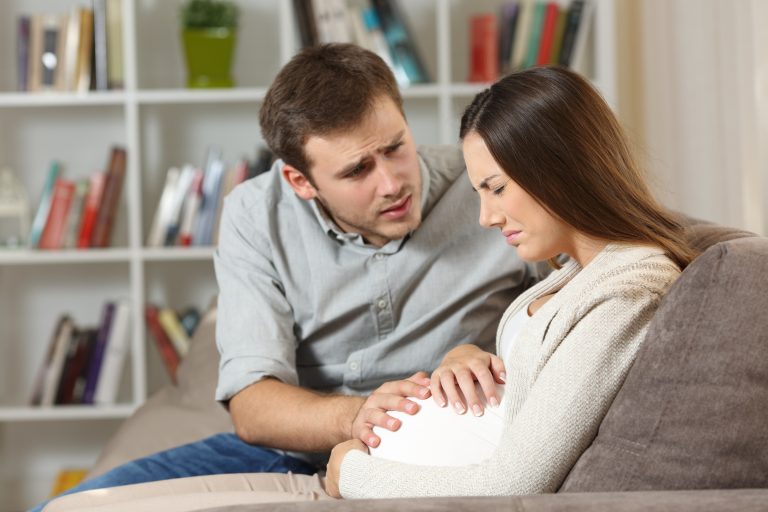 Pregnant woman with epilepsy experiencing discomfort while partner provides comfort and support at home