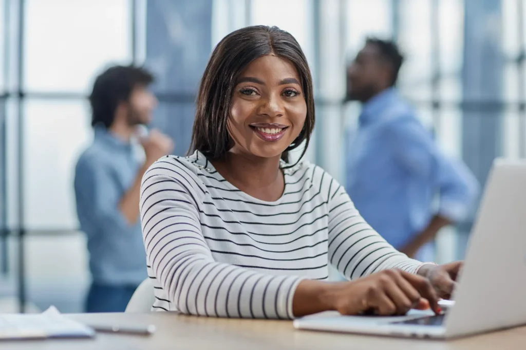 Smiling Black woman employee with epilepsy working on laptop at office desk showing workplace inclusion and support