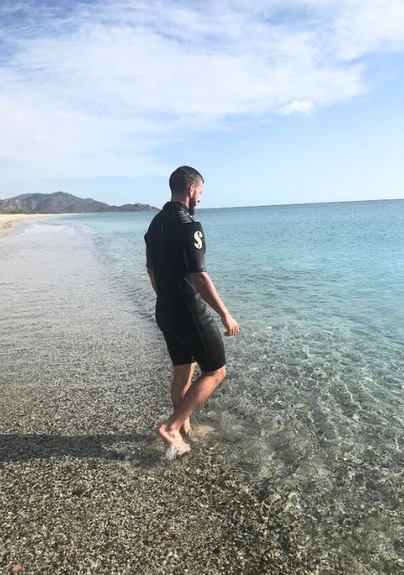 Anze standing in ocean waves at scenic Scottish beach sharing his epilepsy story and journey