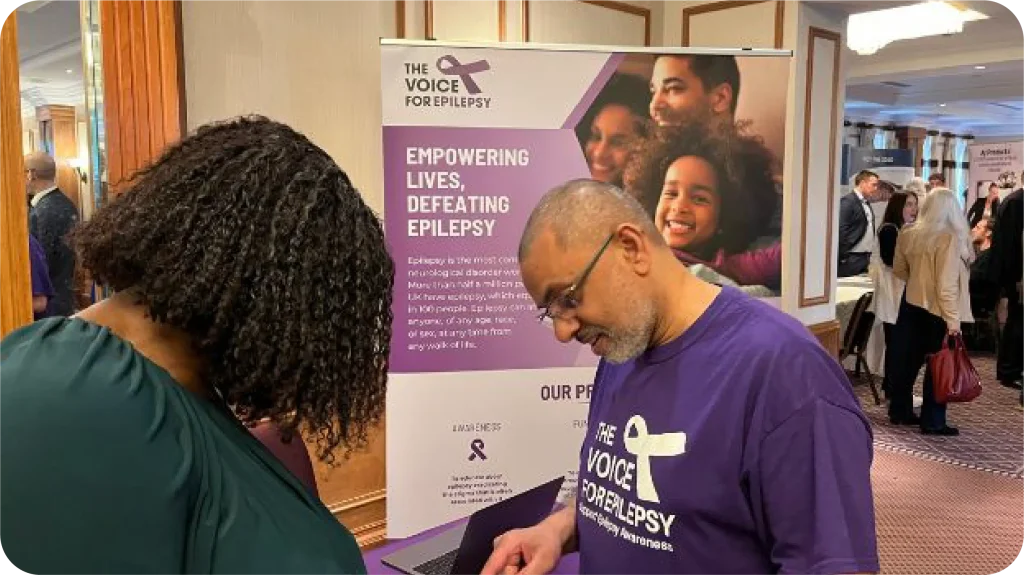 The Voice For Epilepsy awareness event with supporter wearing purple charity t-shirt next to banner reading Empowering Lives Defeating Epilepsy