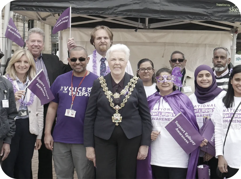 Group of supporters at National Epilepsy Awareness Week event wearing purple and holding awareness flags