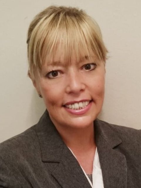 Professional portrait of a woman with blonde hair wearing a gray blazer and smiling at the camera.