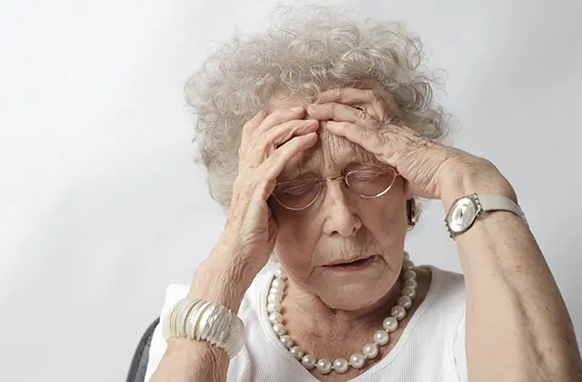 Elderly woman holding her head experiencing discomfort or warning signs