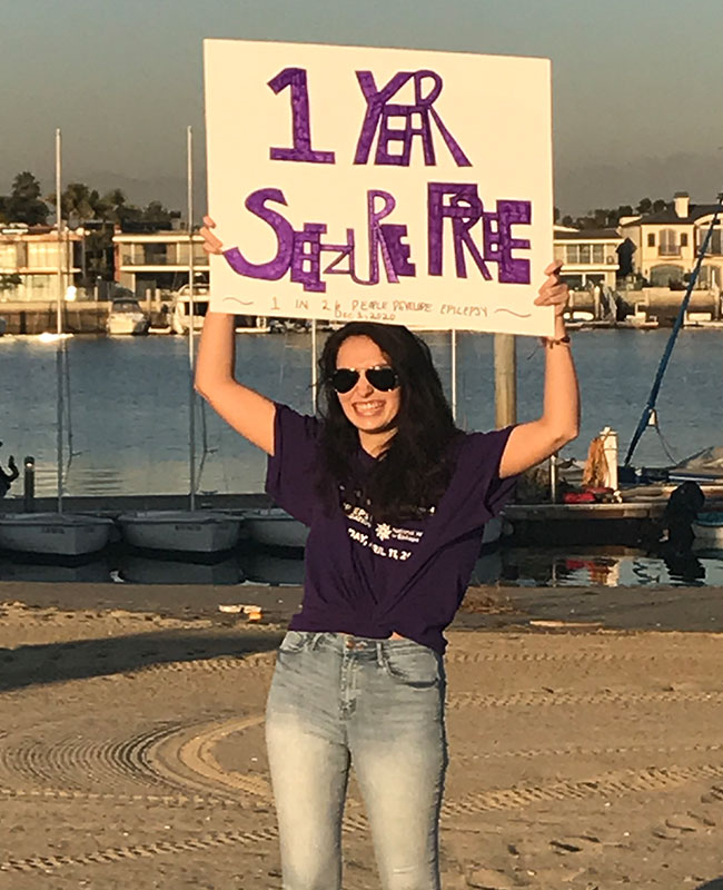 Addison Taylor celebrating being seizure-free, holding a celebratory sign outdoors