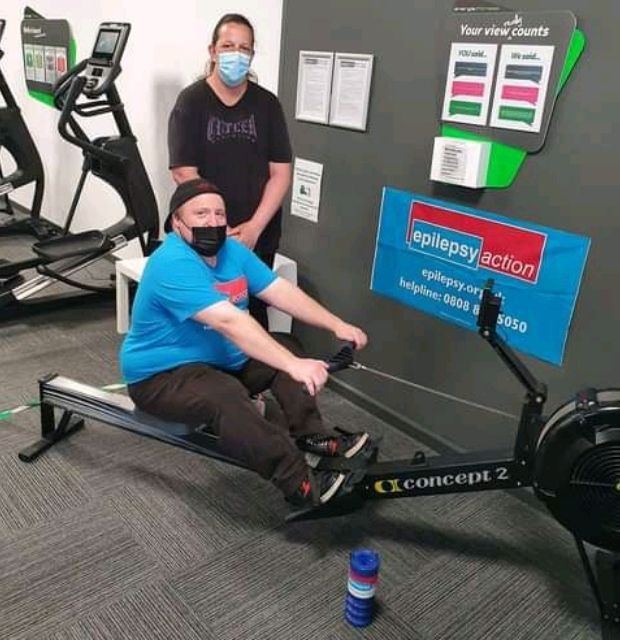 Jonathan working out on rowing machine at gym with Epilepsy Action supporter, showing active lifestyle with epilepsy